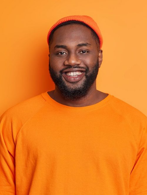 waist-up-shot-of-happy-black-man-smiles-happily-dressed-in-orange-hat-and-sweater-being-in-good-mood-e1627313512303.jpg